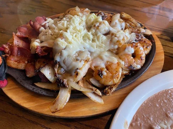 A sizzling platter of shrimp and meat topped with cheese